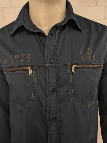 Devinez la chemise en jeans. Bleu foncé coloré avec des accents à fermeture éclair avec des sacs à poitrine. Taille L.
