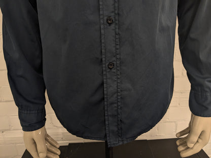 Devinez la chemise en jeans. Bleu foncé coloré avec des accents à fermeture éclair avec des sacs à poitrine. Taille L.