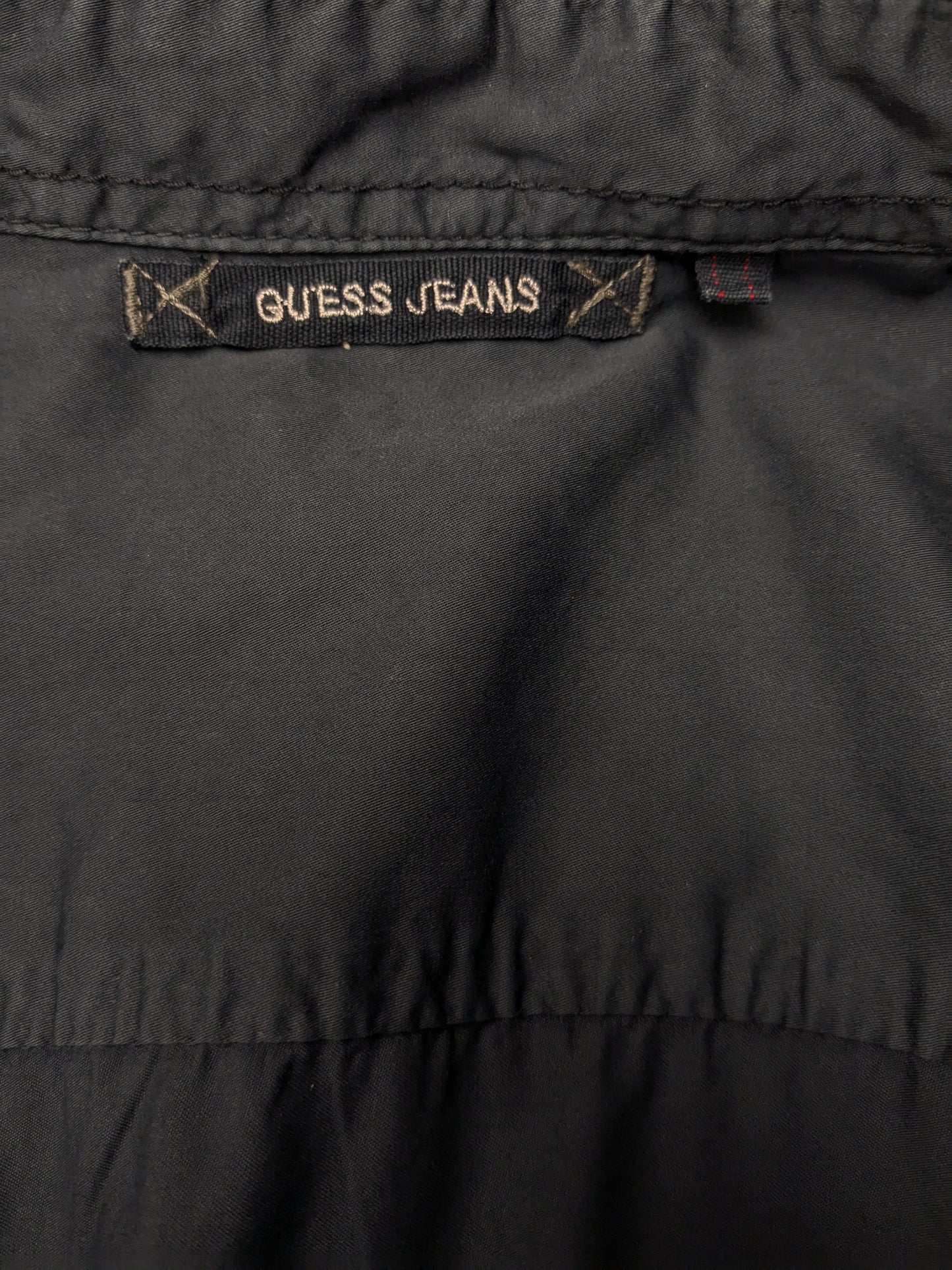 Devinez la chemise en jeans. Bleu foncé coloré avec des accents à fermeture éclair avec des sacs à poitrine. Taille L.