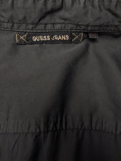 Devinez la chemise en jeans. Bleu foncé coloré avec des accents à fermeture éclair avec des sacs à poitrine. Taille L.